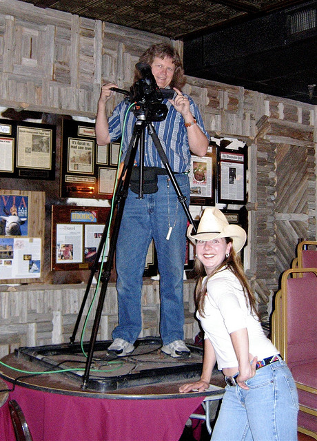 Woman in cowboy hat stands next to videographer with camera 